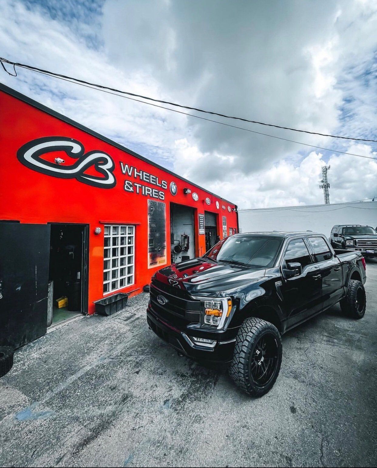 A black truck is parked in front of a red building. | CB Wheels & Tires, 4x4, Suspension, Center