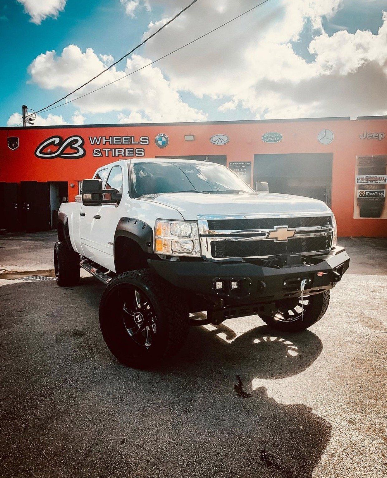 A white truck is parked in front of a car dealership. | CB Wheels & Tires, 4x4, Suspension, Center