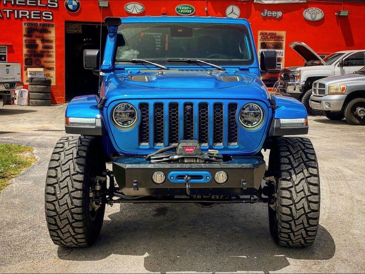 A blue jeep is parked in front of a red building. | CB Wheels & Tires, 4x4, Suspension, Center
