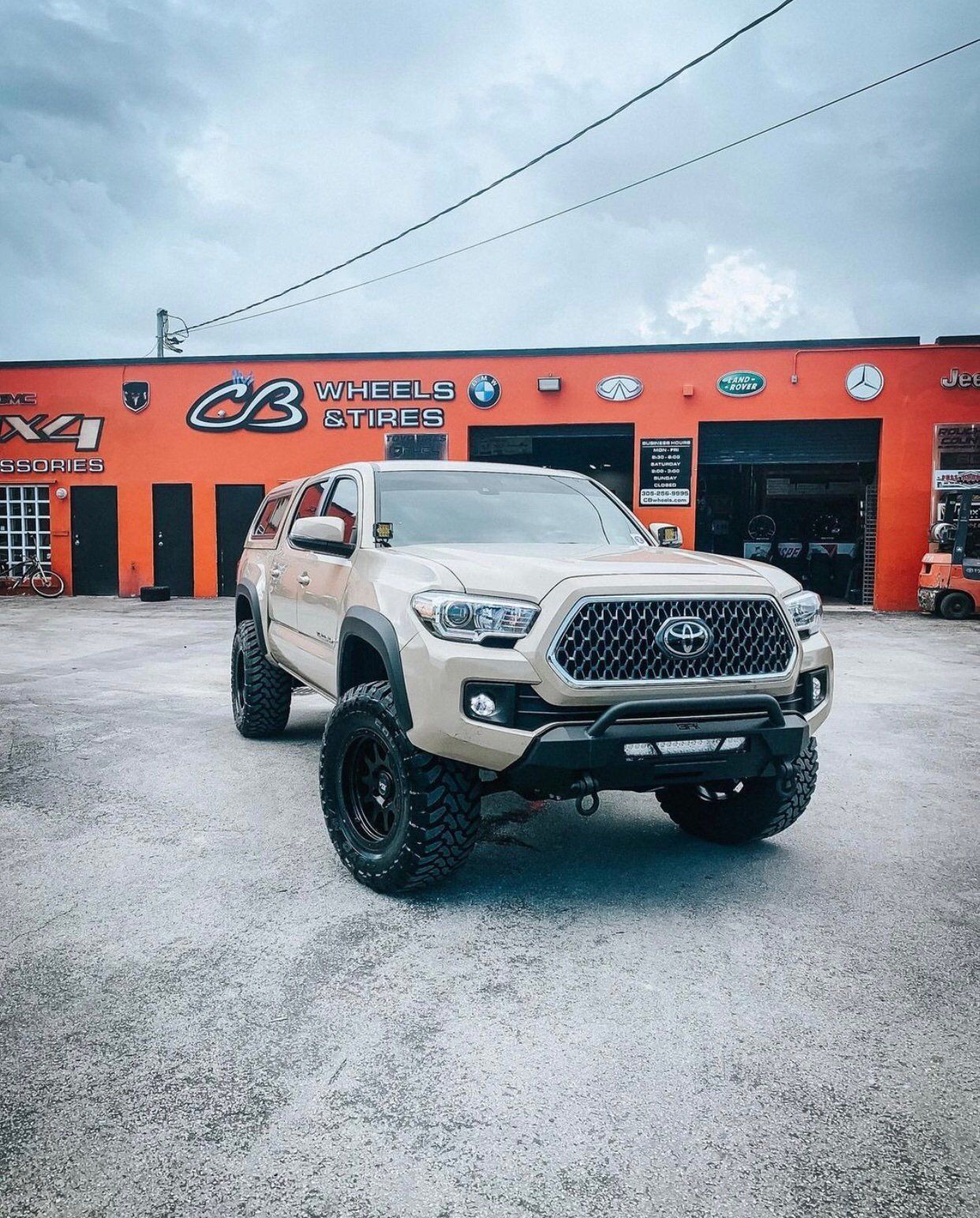 A white truck is parked in front of an orange building. | CB Wheels & Tires, 4x4, Suspension, Center