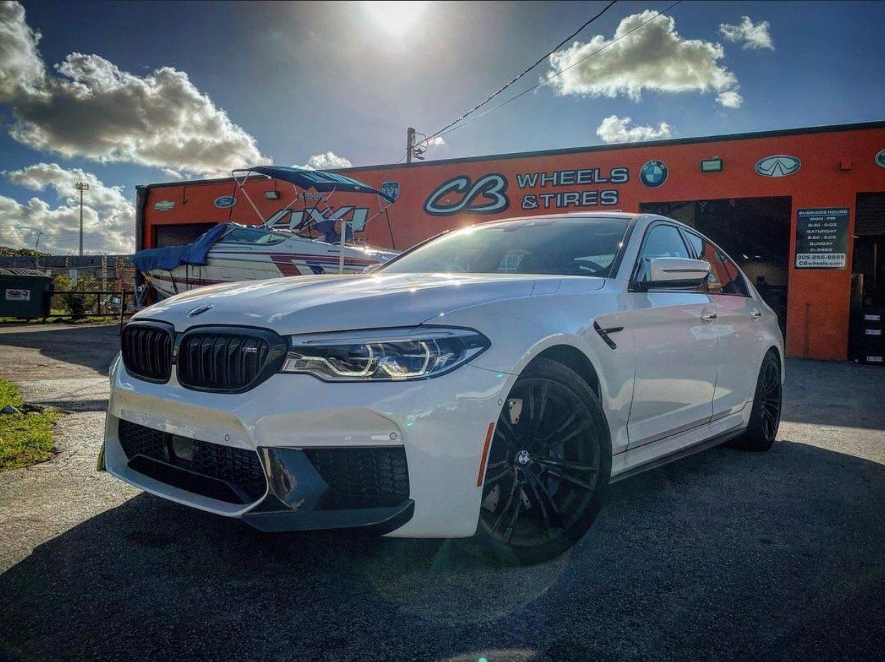 A white bmw m5 is parked in front of a car dealership. | CB Wheels & Tires, 4x4, Suspension, Center