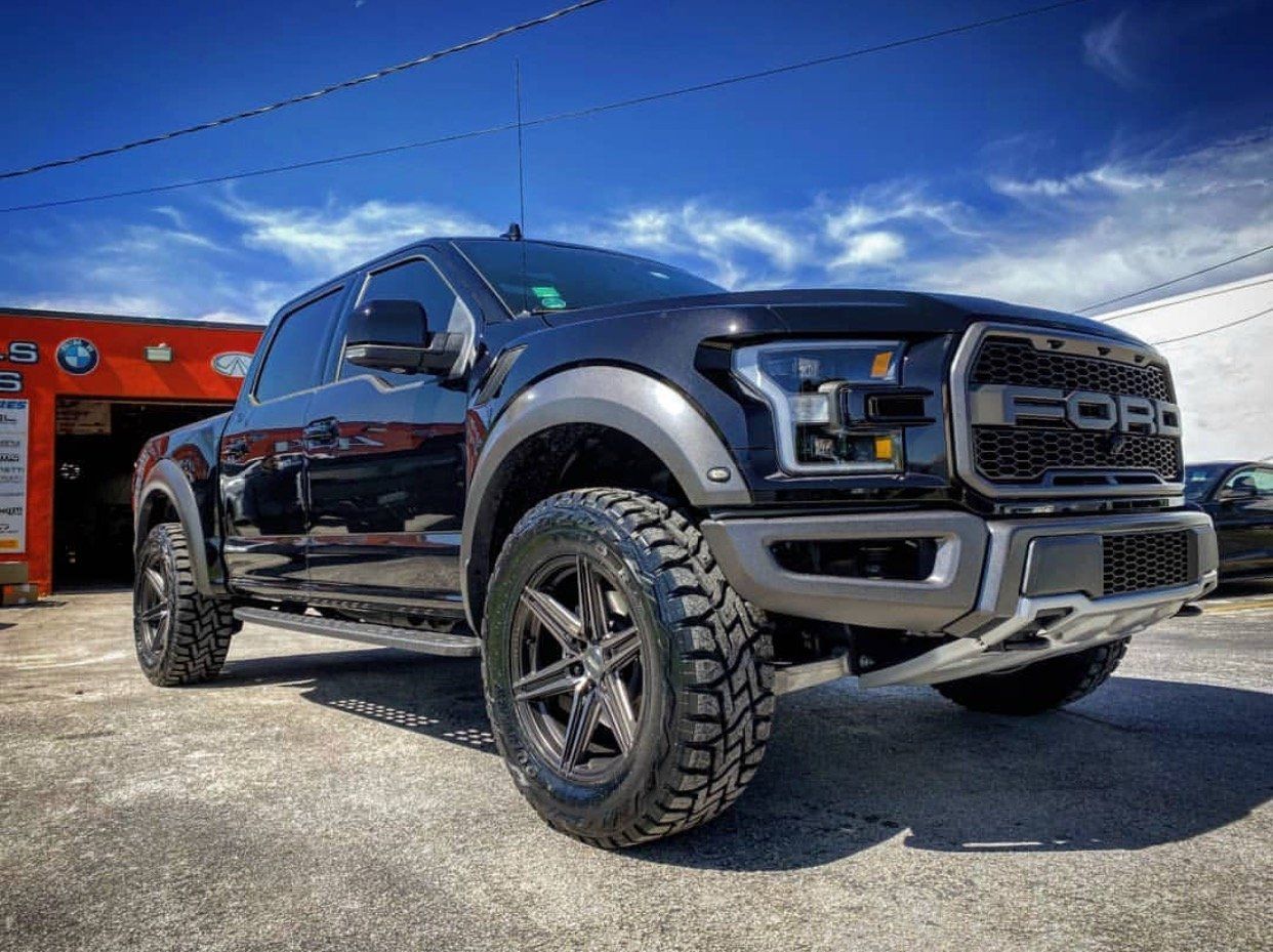A black ford raptor is parked in front of a garage. | CB Wheels & Tires, 4x4, Suspension, Center