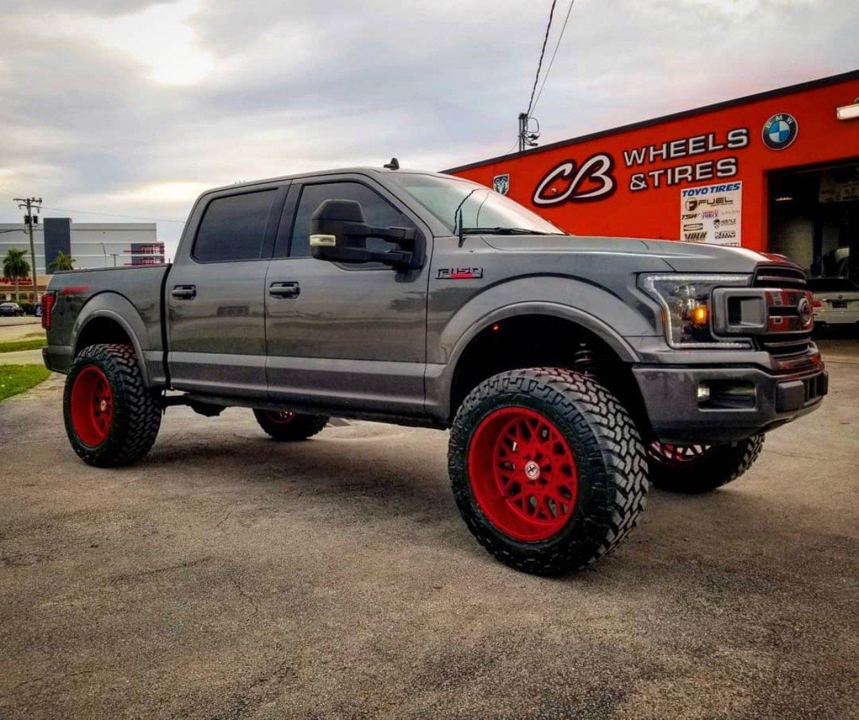 A gray truck with red wheels is parked in front of a cb wheels and tires store. | CB Wheels & Tires, 4x4, Suspension, Center