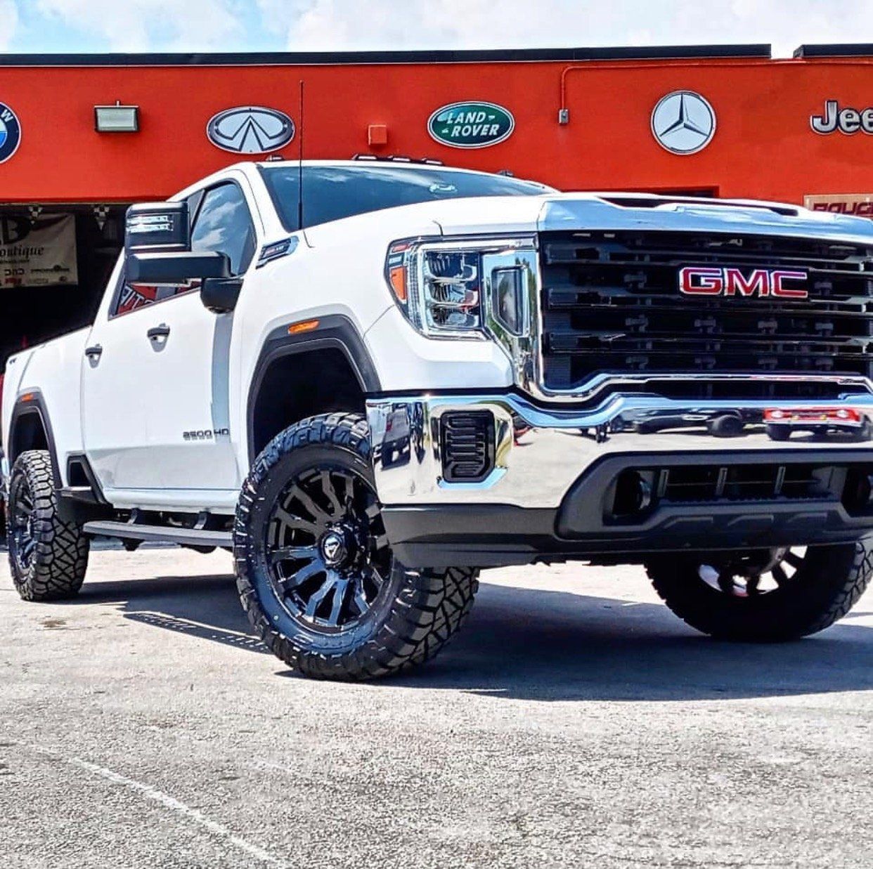 A white gmc truck is parked in front of a red building. | CB Wheels & Tires, 4x4, Suspension, Center