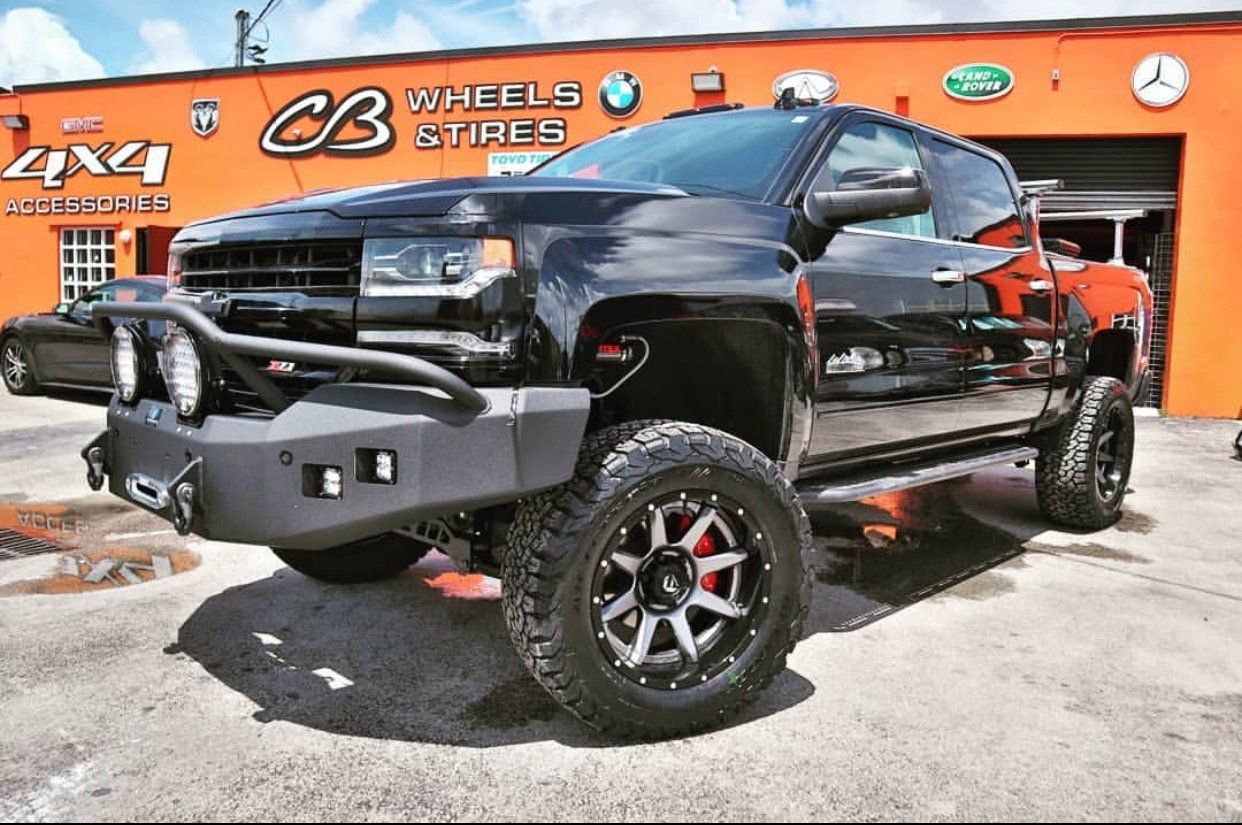 A black truck is parked in front of an orange building. | CB Wheels & Tires, 4x4, Suspension, Center