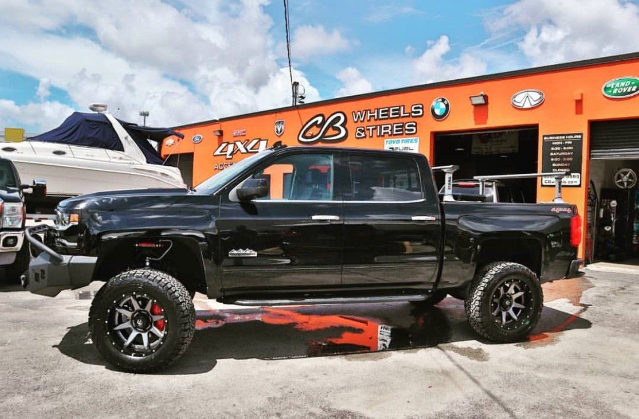 A black truck is parked in front of an orange building. | CB Wheels & Tires, 4x4, Suspension, Center