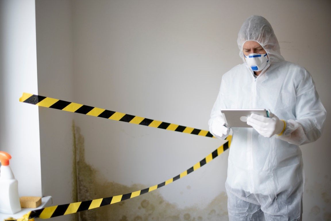 Mold inspector with tablet standing behind yellow caution tape.