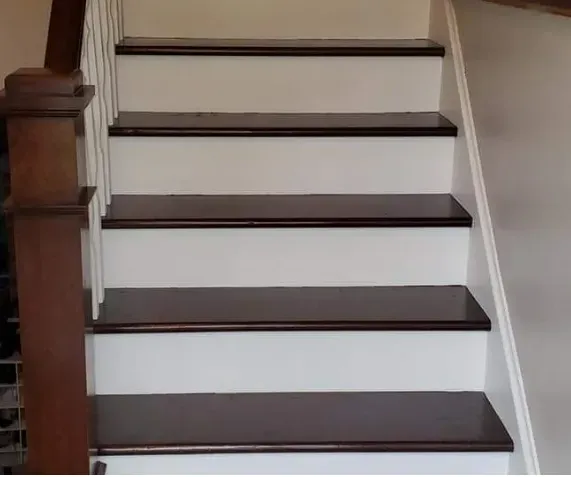 Staircase with dark wood treads and white risers, leading upward. Brown banister on left.