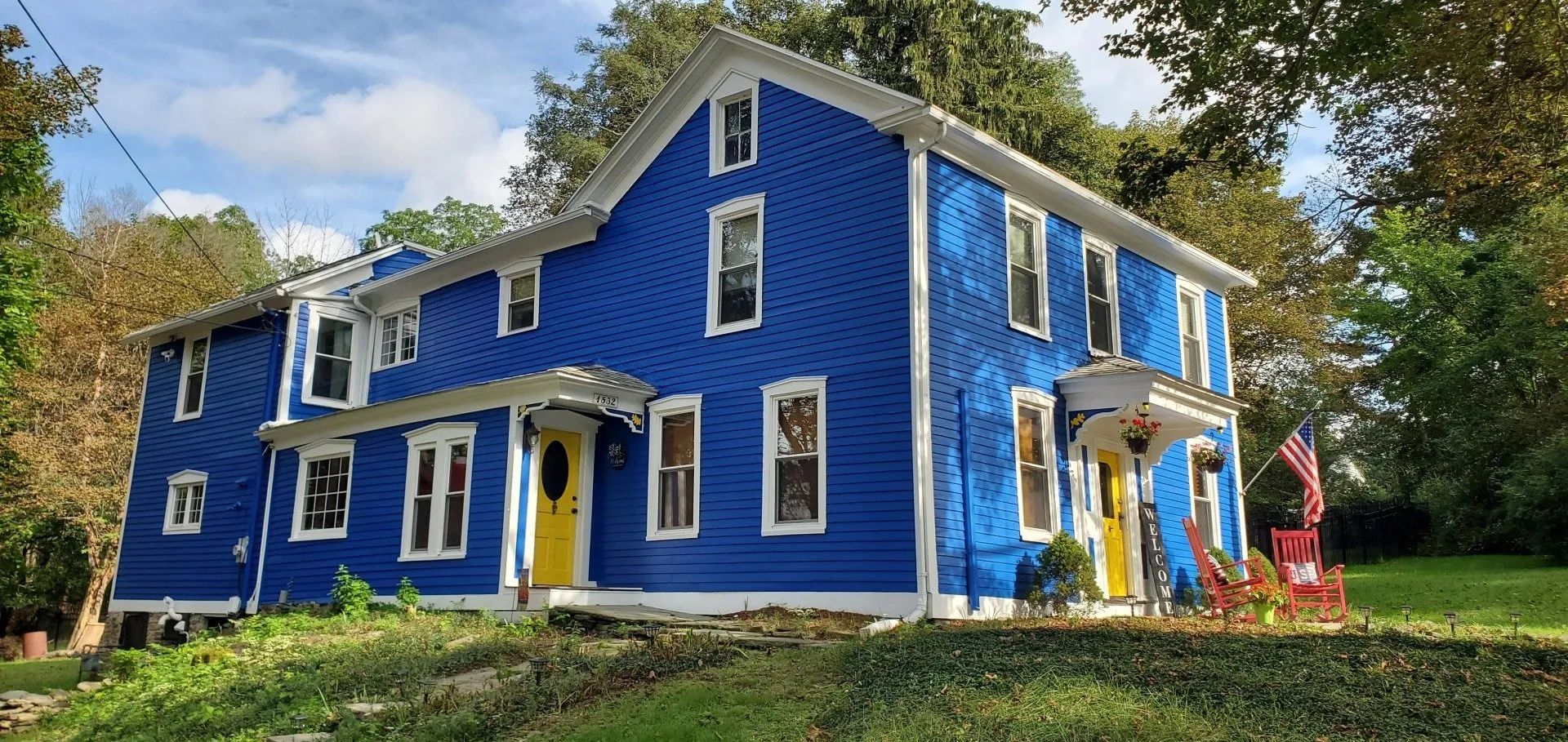Blue house with yellow doors, white trim, and American flag.
