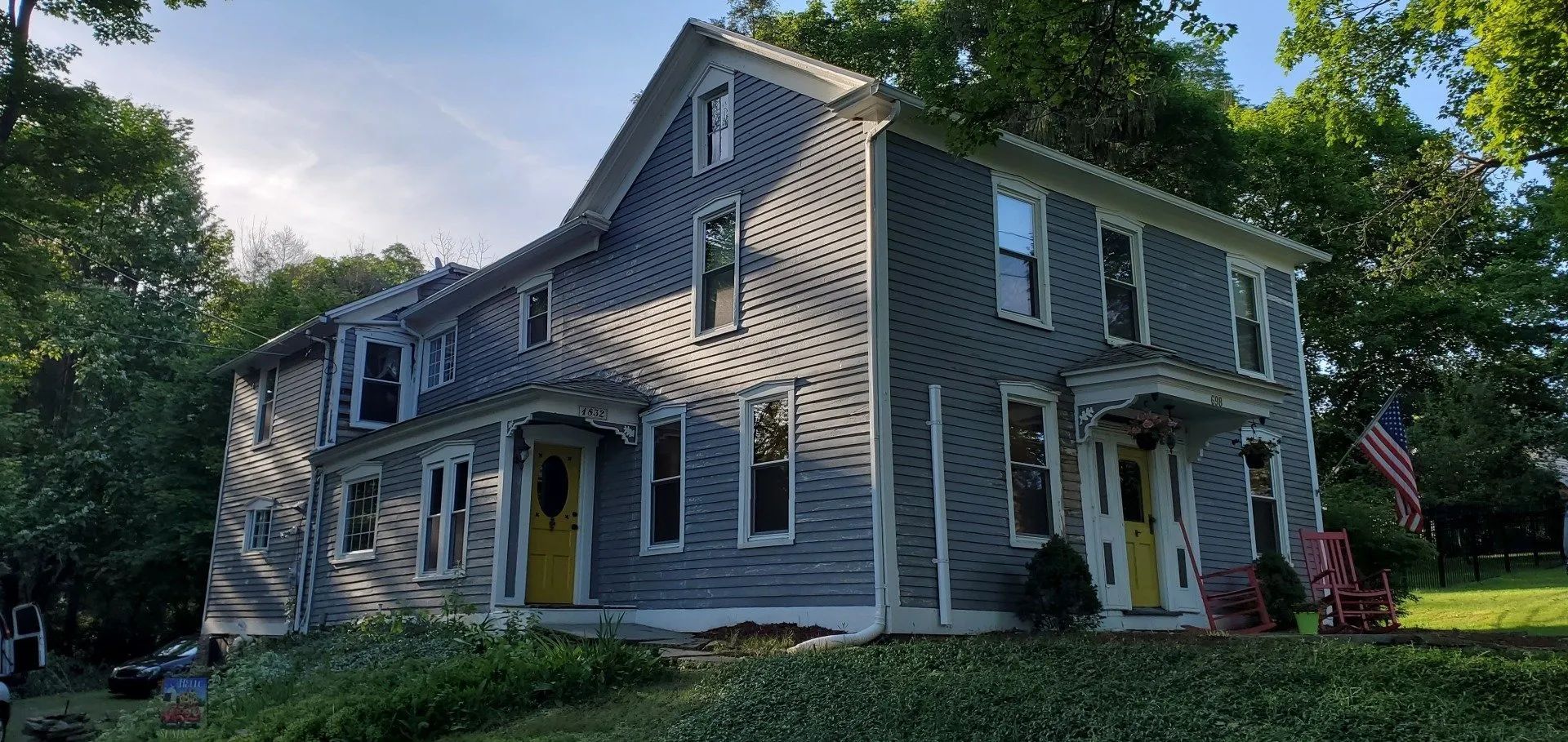 Two-story gray house with yellow front doors and an American flag on the lawn.