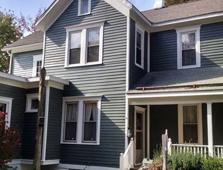 Two-story gray house with yellow front doors and an American flag on the lawn.