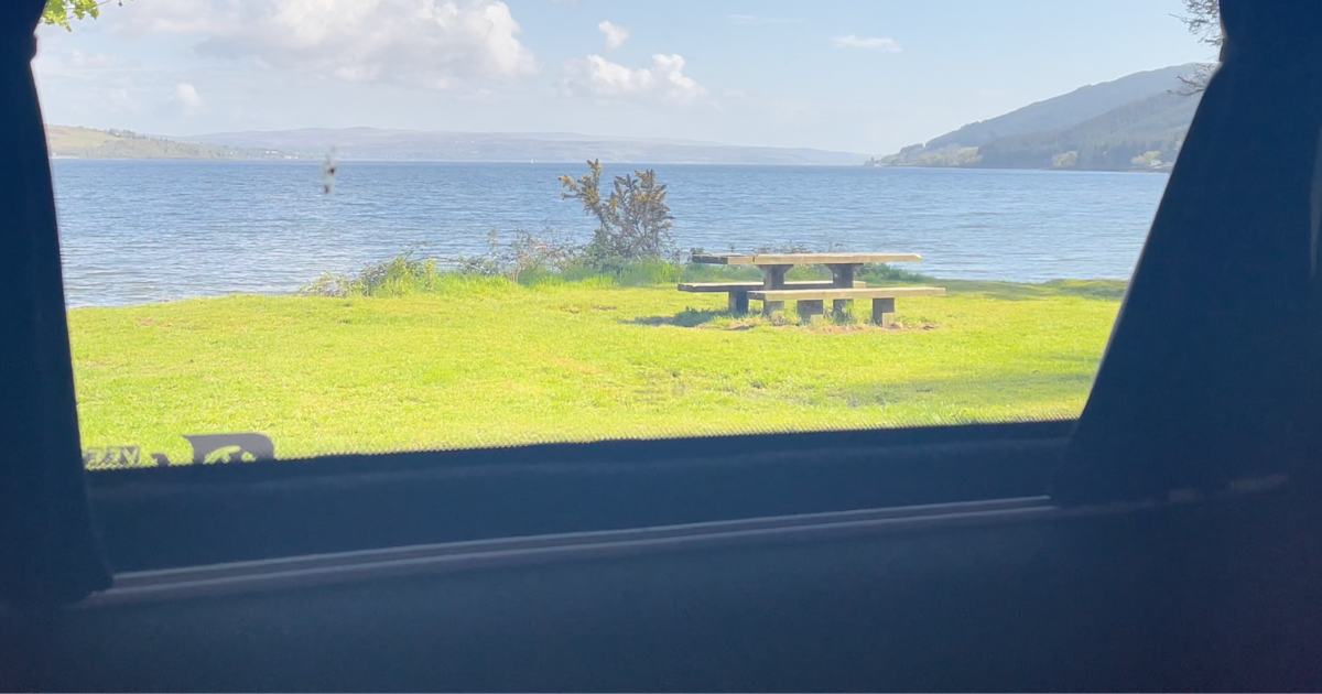 A view of a picnic table and a lake from a car window.