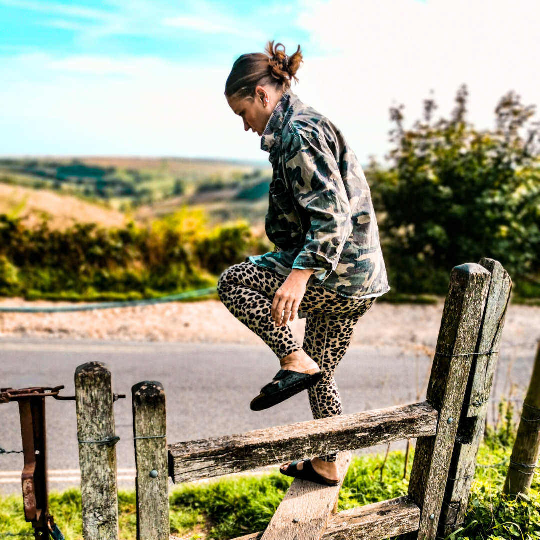 A woman in leopard print pants is walking across a wooden fence.