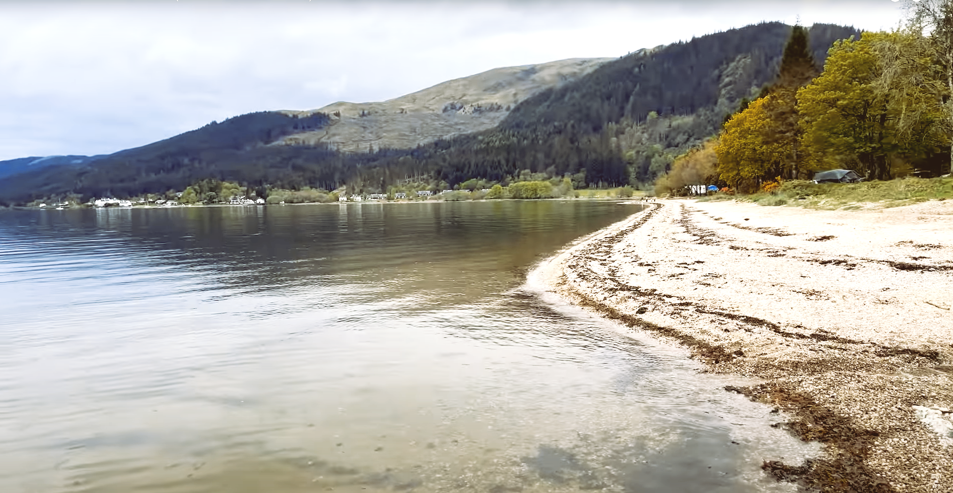 A lake with mountains in the background and a sandy beach in the foreground.