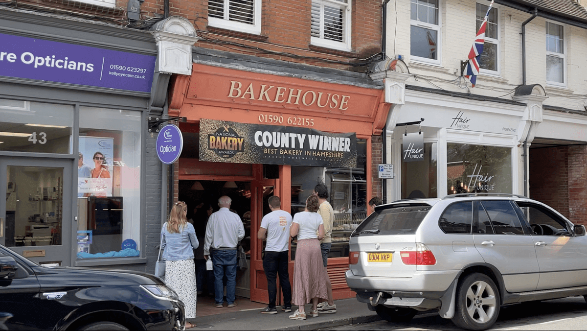 A group of people are standing outside of a bakery.