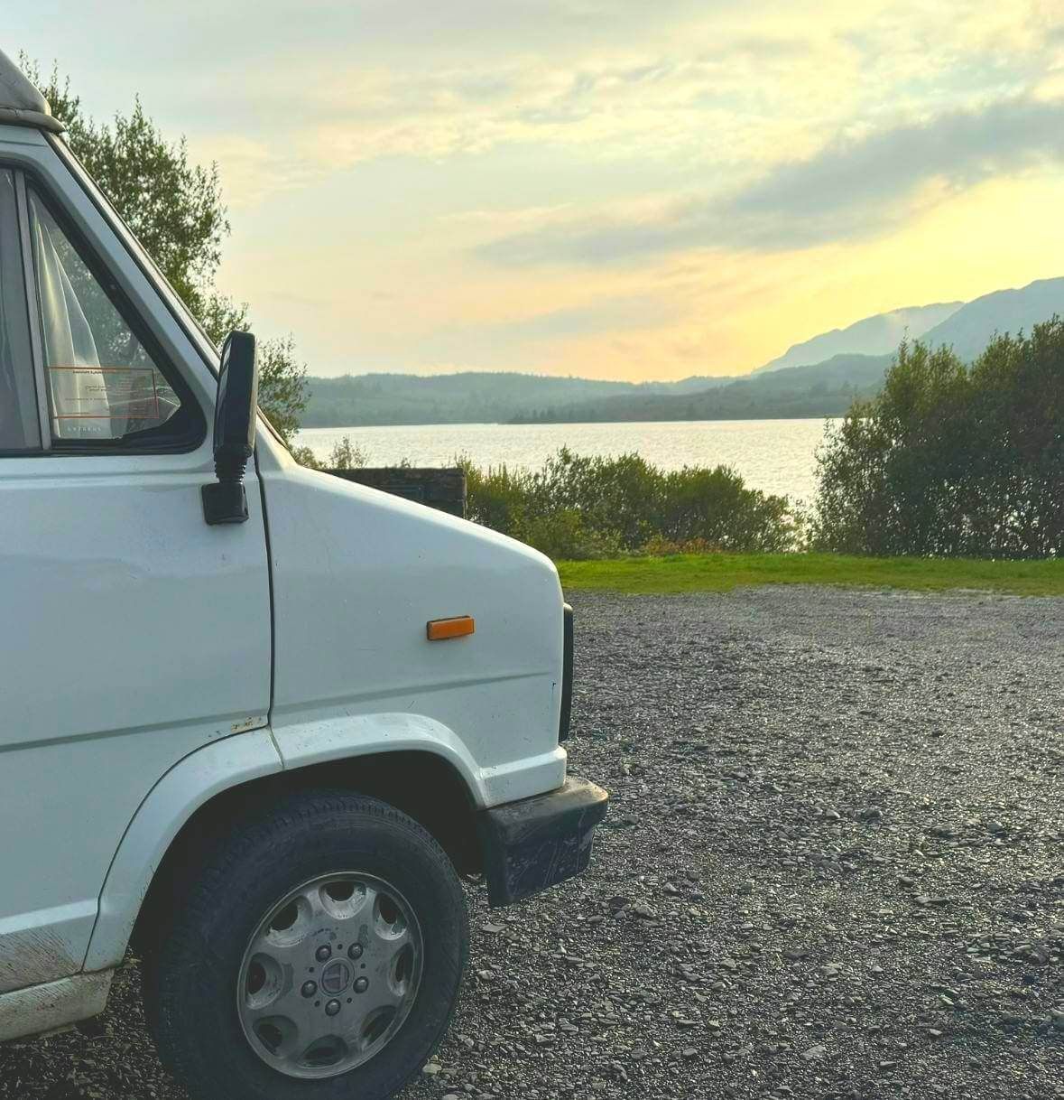 A white van is parked on gravel near a lake