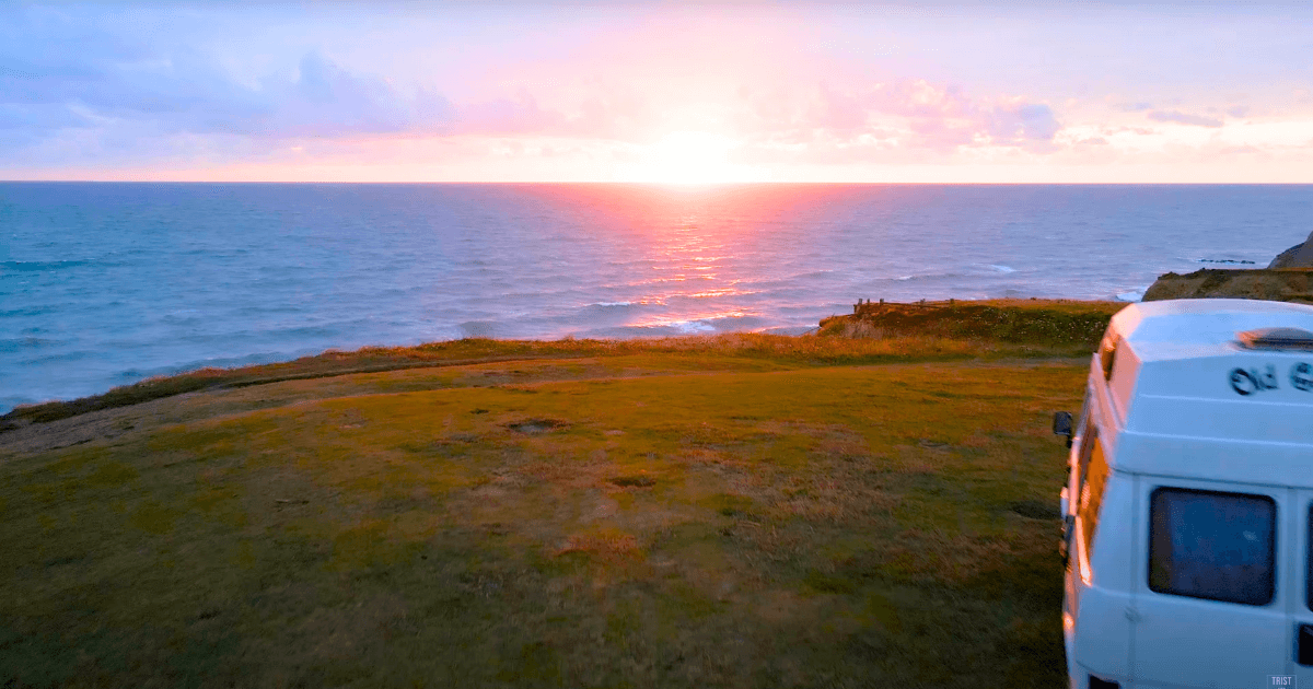 a camper van is parked on a cliff overlooking the ocean at sunset.