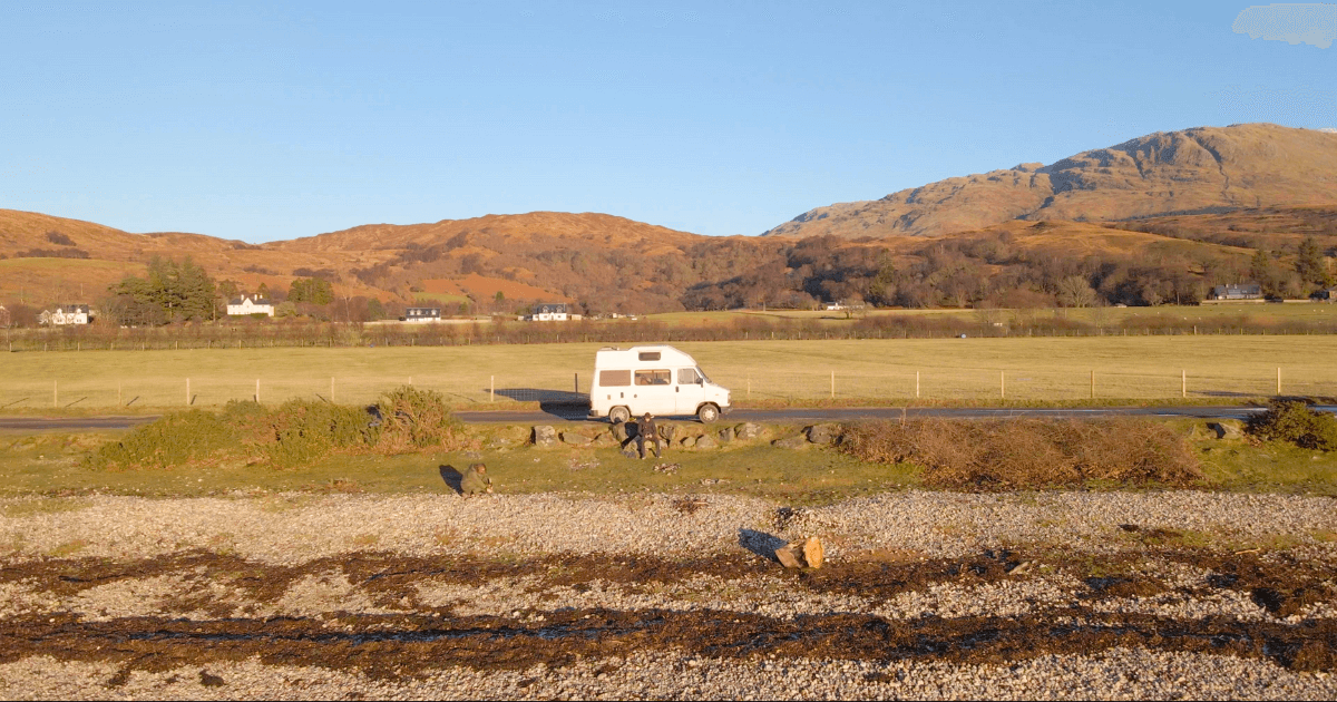 A white van is driving down a road with mountains in the background.