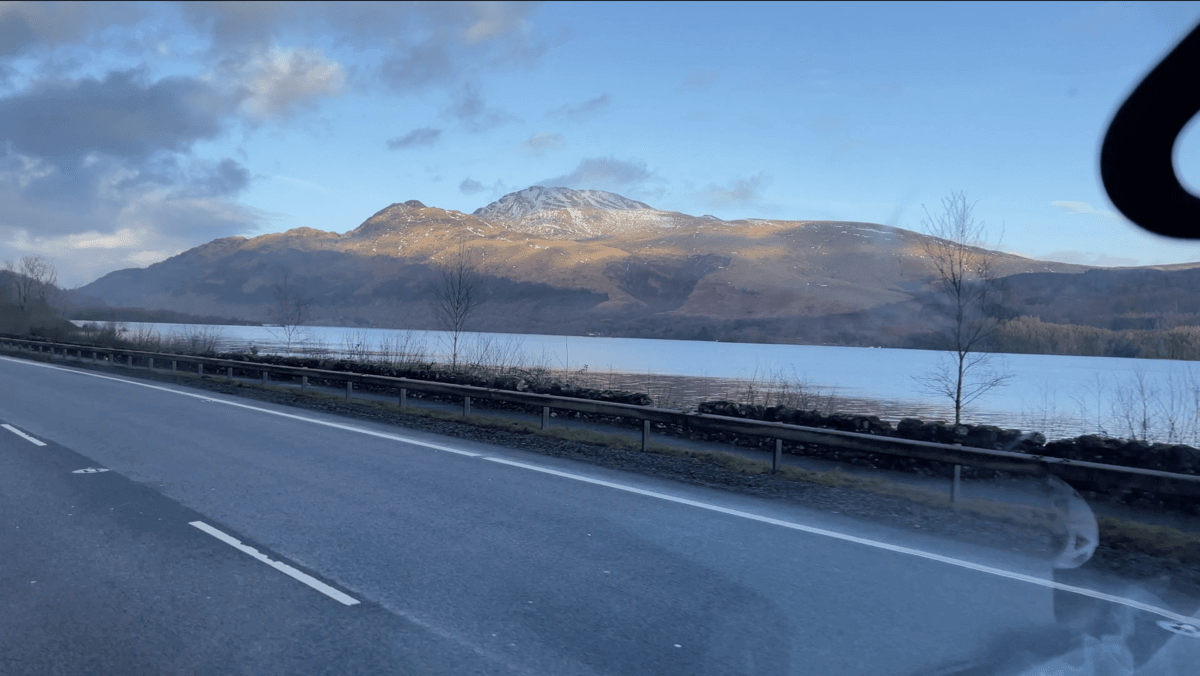 Driving down a road next to a lake with mountains in the background.