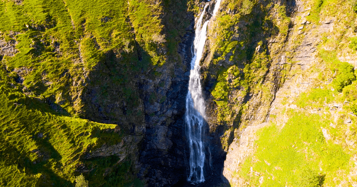 An aerial view of a waterfall in the mountains surrounded by trees.