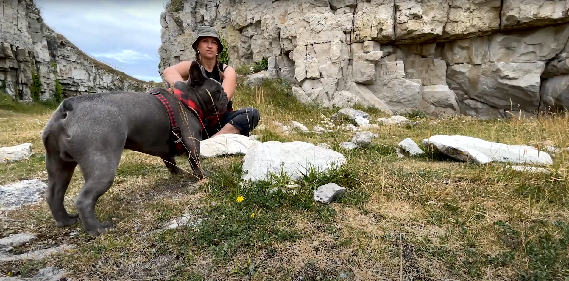 A woman is sitting down next to a dog at Winspit Quarry.