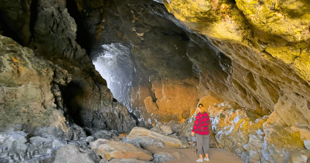 a woman in a red jacket is standing in merlins cave.