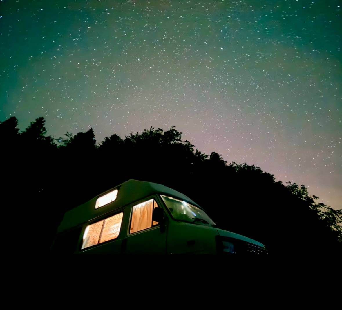 A camper van is parked under a starry night sky