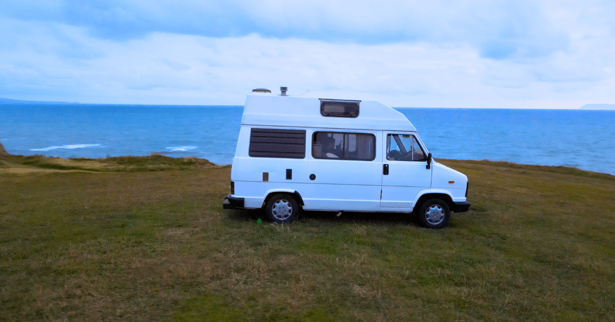 a white camper van is parked on a grassy hill near the ocean .