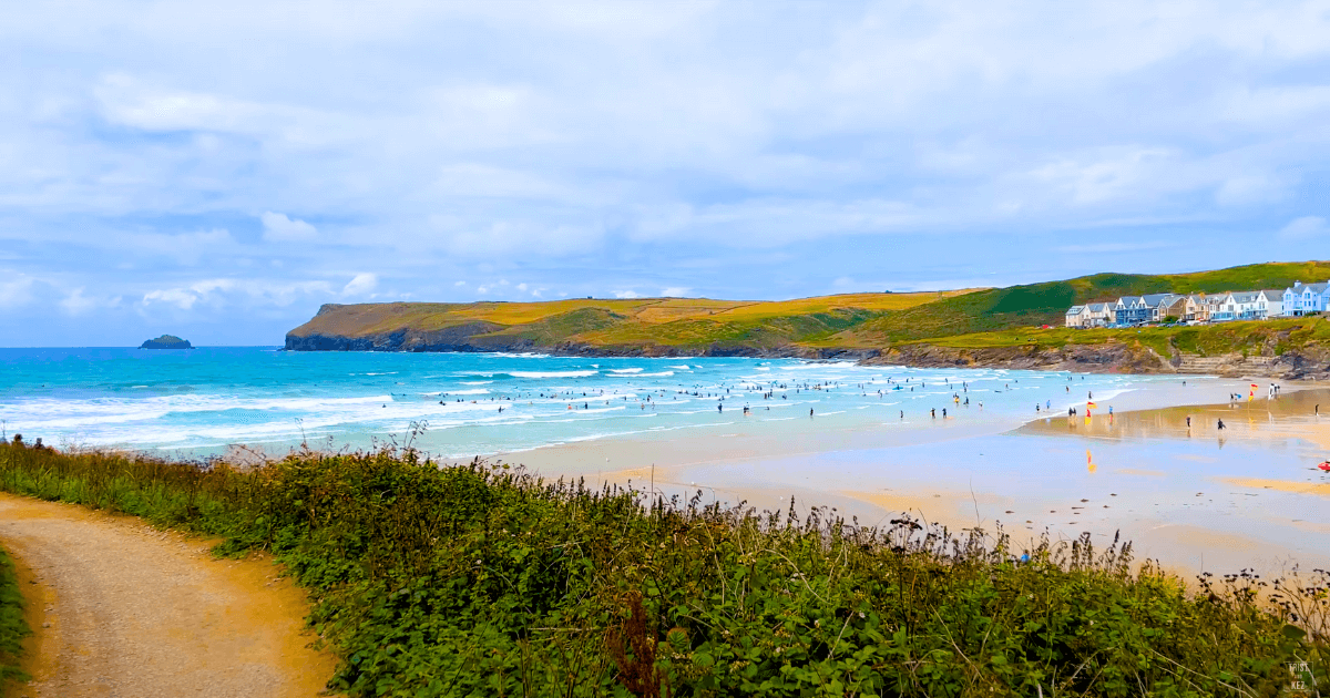 a path leading to Polzeath beach with people swimming in the ocean.