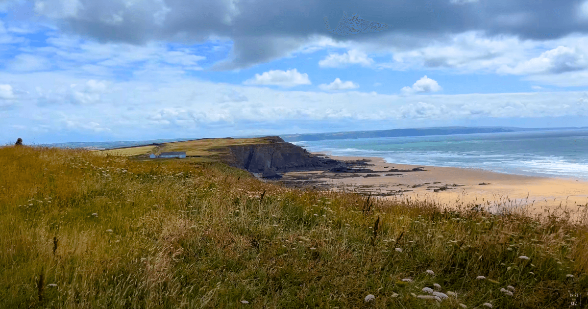 a view of a beach from a grassy hill and beach on a cloudy day.