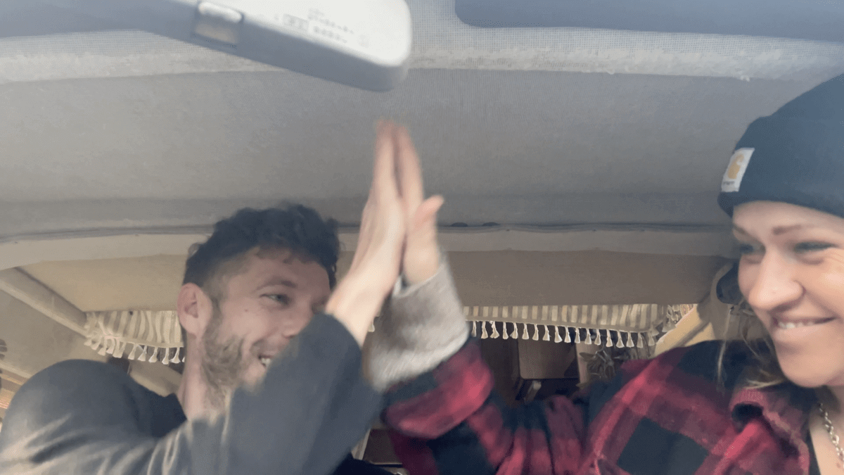 Trist and Kez are giving each other a high-five in a van.