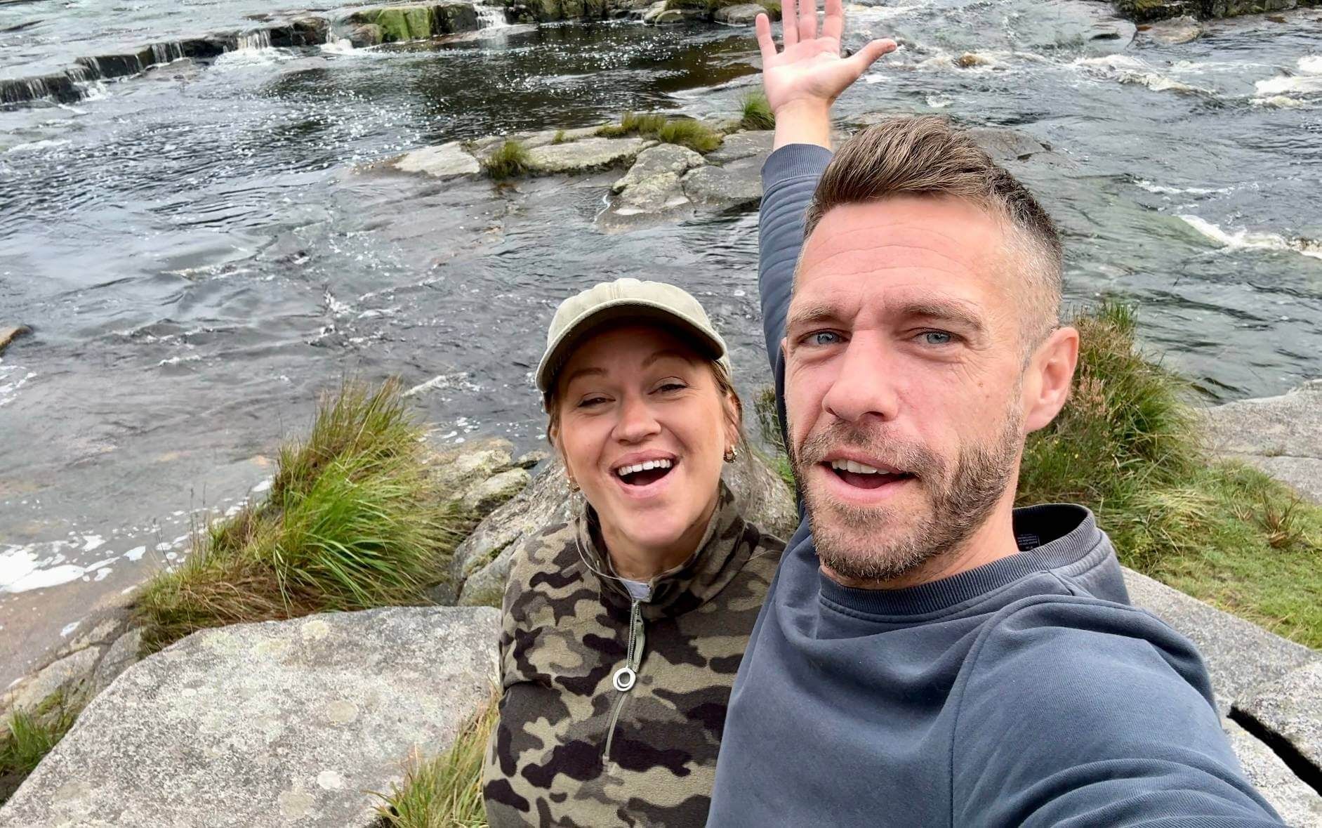 A man and a woman are taking a selfie in front of a river.