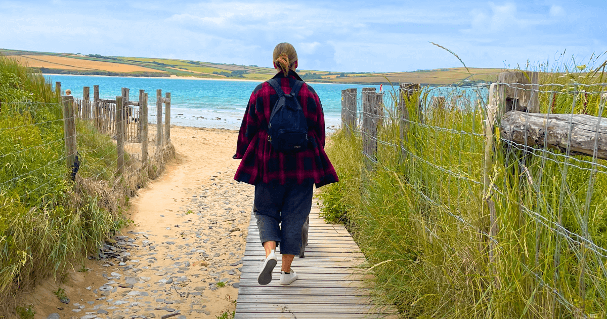 a woman is walking down a wooden path to the beach.