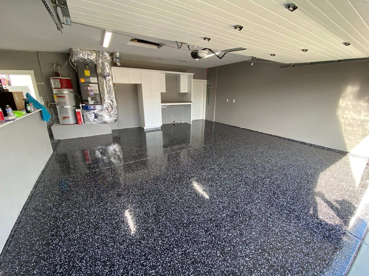 A garage with a black floor and a garage door open.
