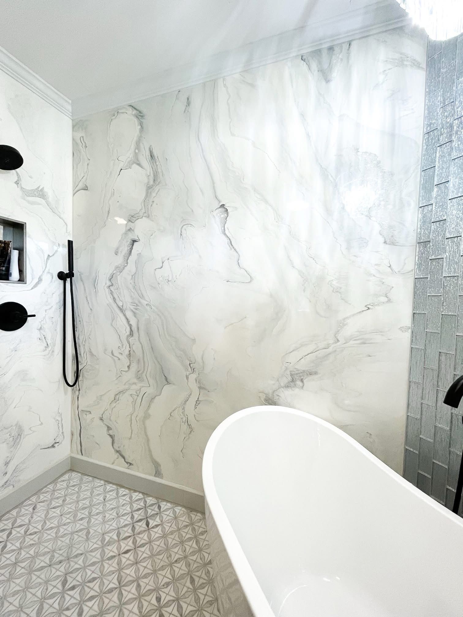 A bathroom with a tub , shower , and marble wall.