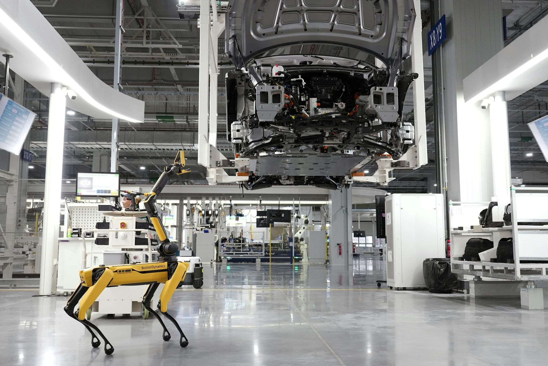 A robot is standing in a factory with a car underneath it.