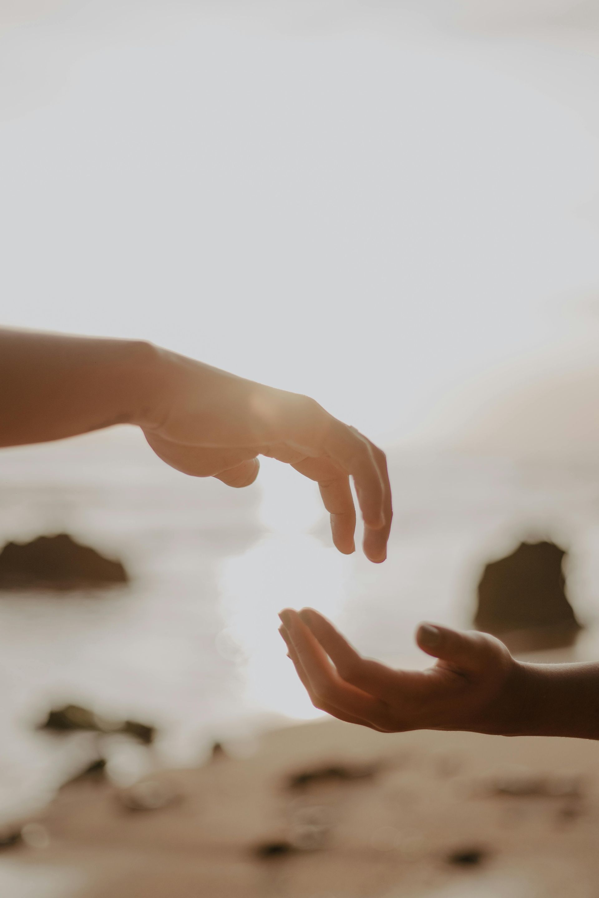 A couple of hands reaching out towards each other on a beach.