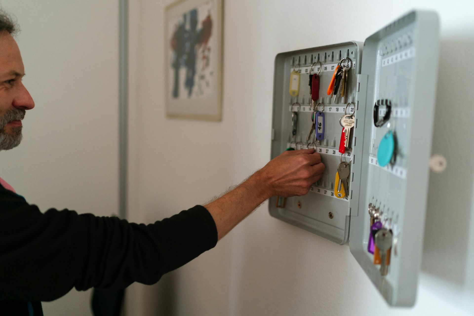 A man is putting keys in a key box on a wall