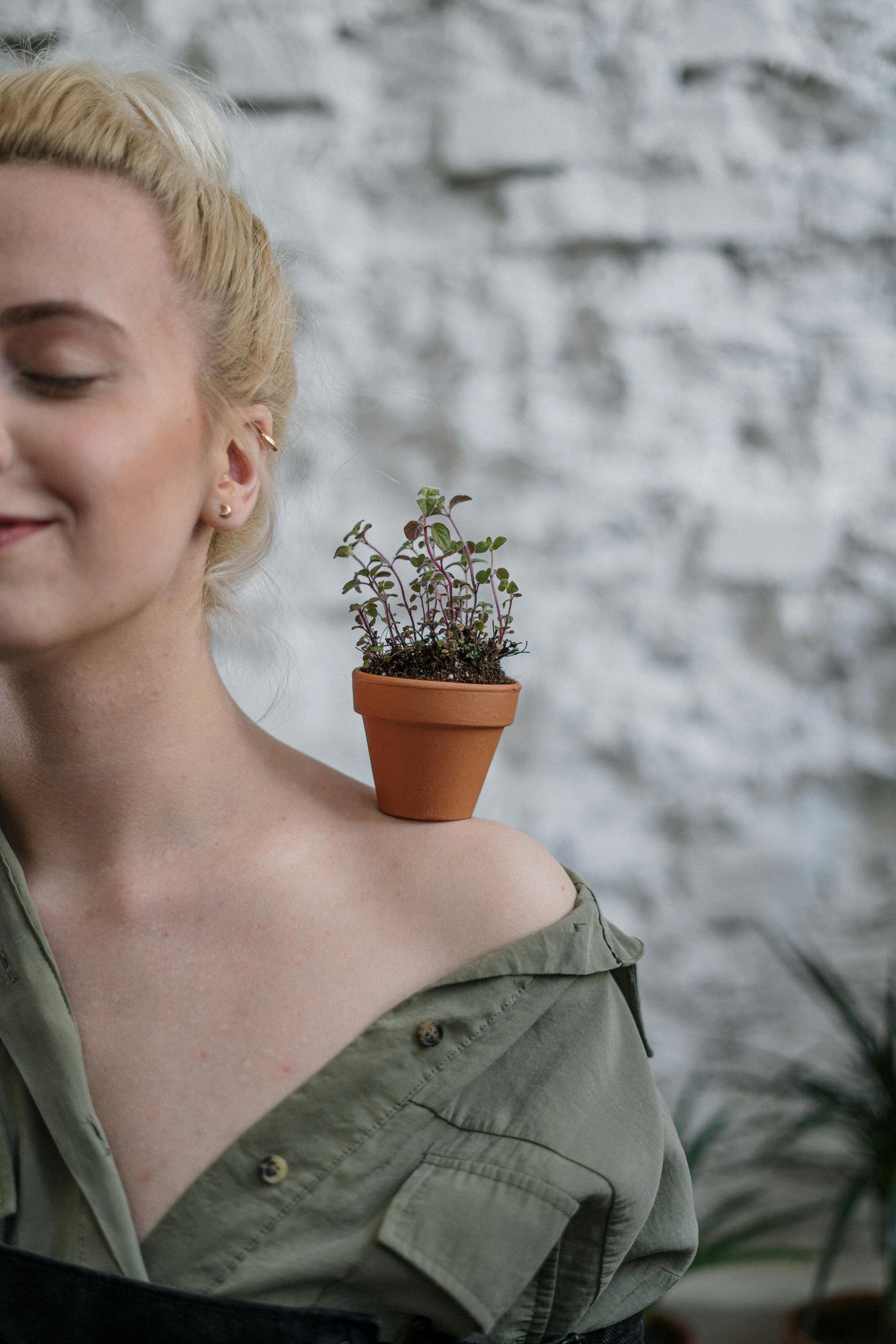 A woman is holding a potted plant on her shoulder.