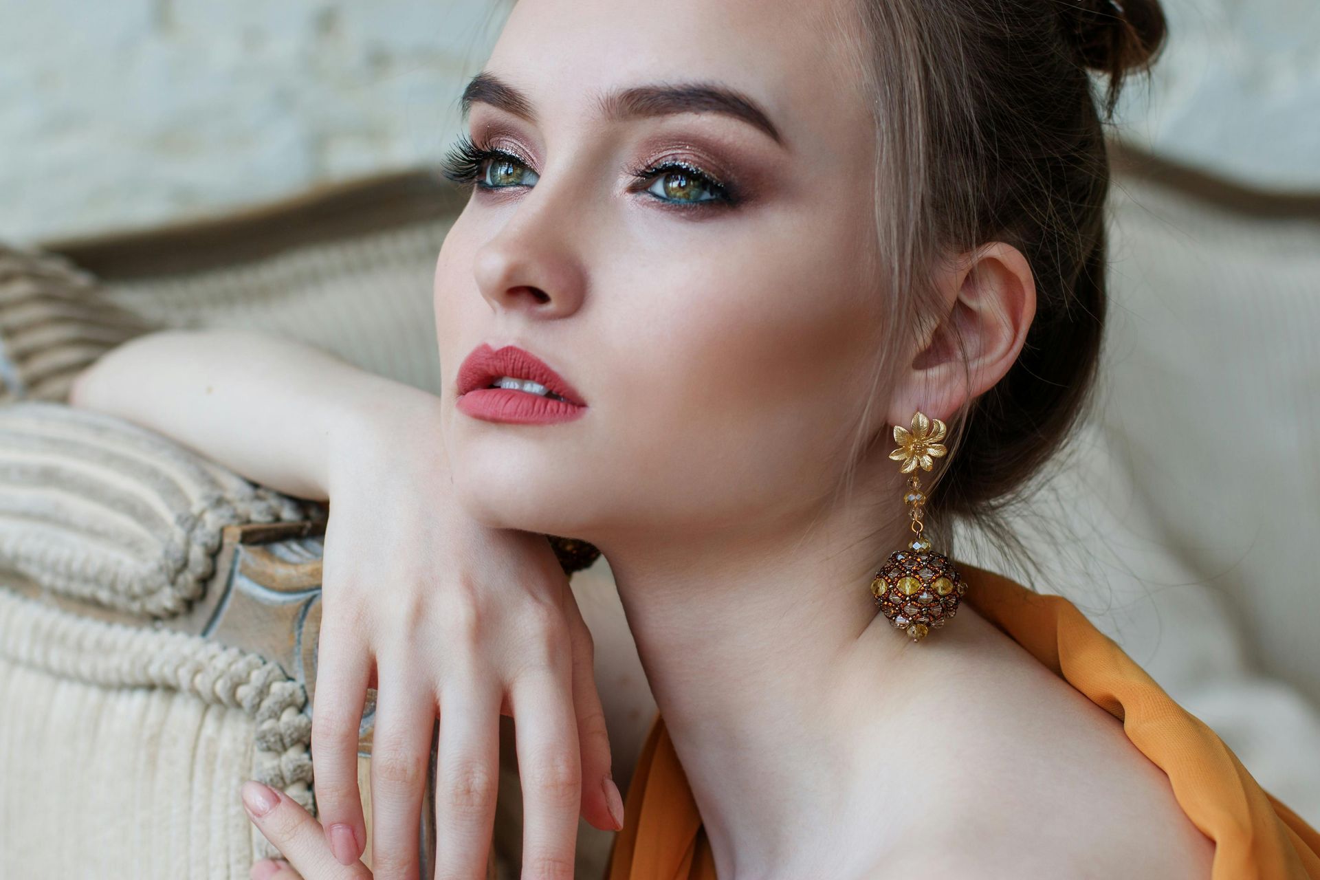 A woman wearing earrings and a bun is sitting on a couch.