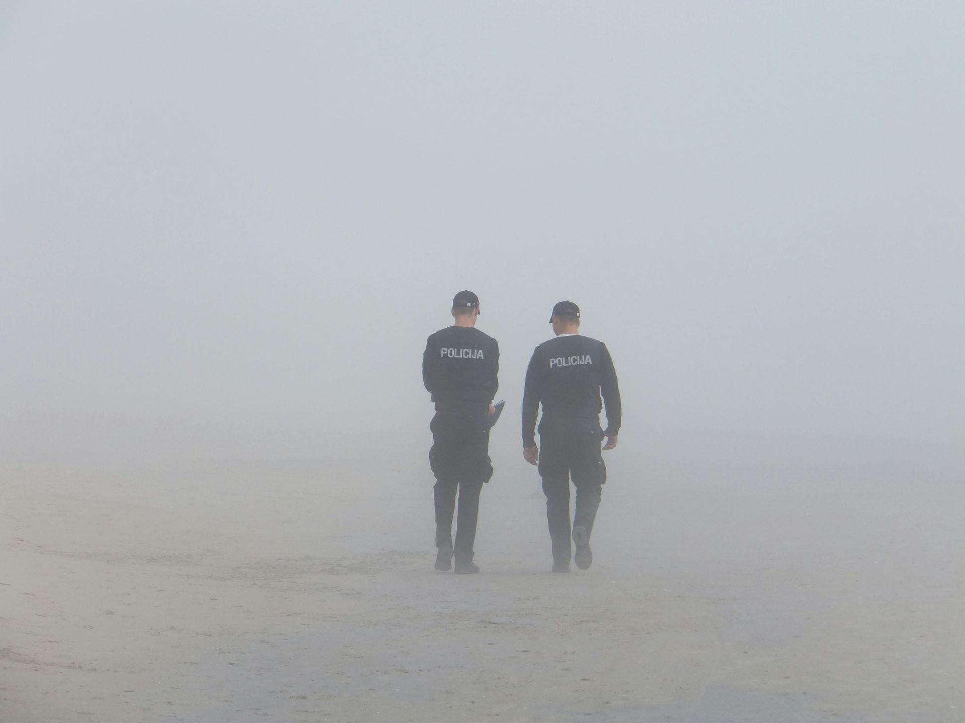 Two police officers are walking in the fog on a beach.
