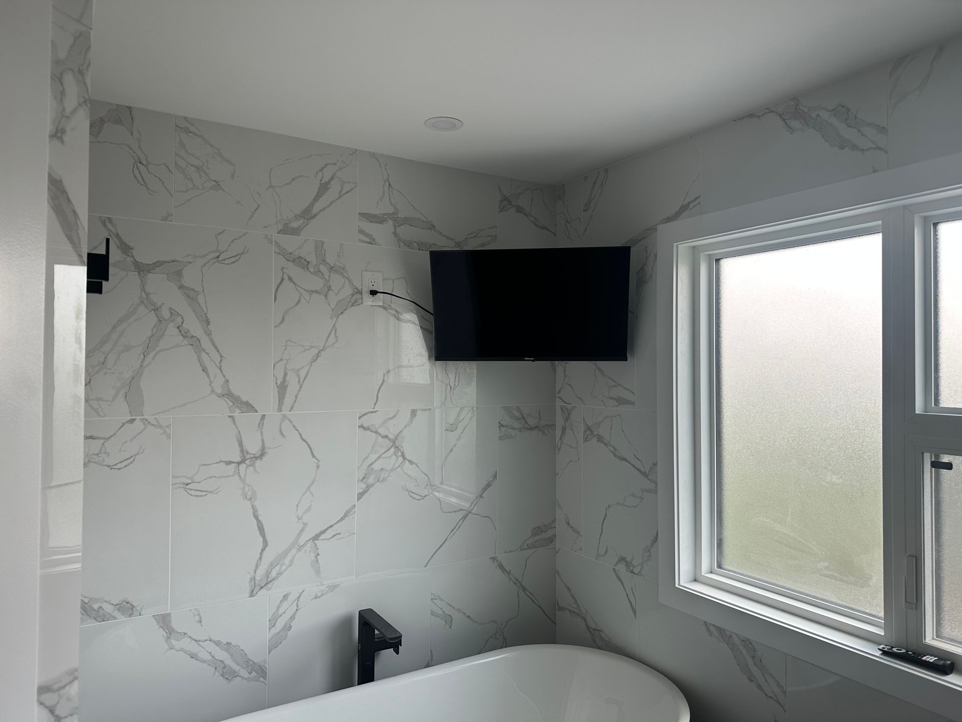 Bathroom with a white sink, tub, and gray tile shower. A doorway leads to a hallway with wood flooring.