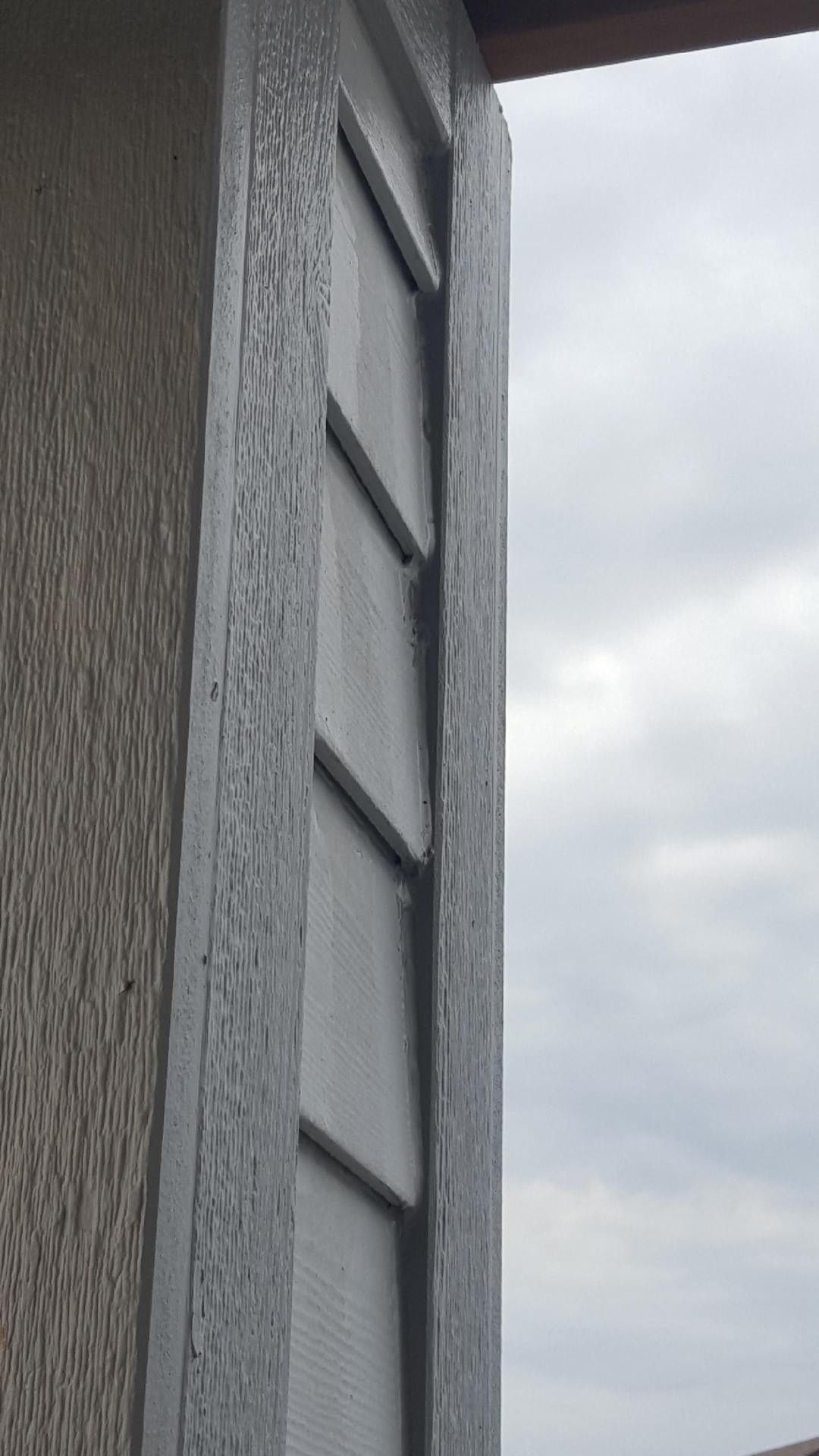 Person installing beige vinyl siding on a building exterior, wearing work gloves and a tool belt.