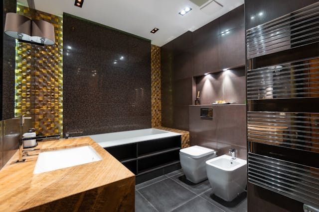 Modern bathroom with gold and brown tiles, white fixtures, and a heated towel rack.