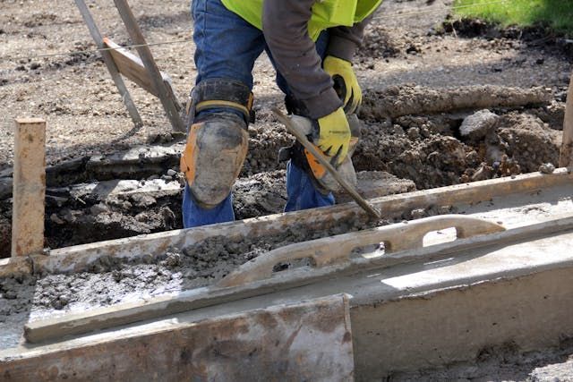 Construction worker smoothing concrete with a trowel in a wooden form.