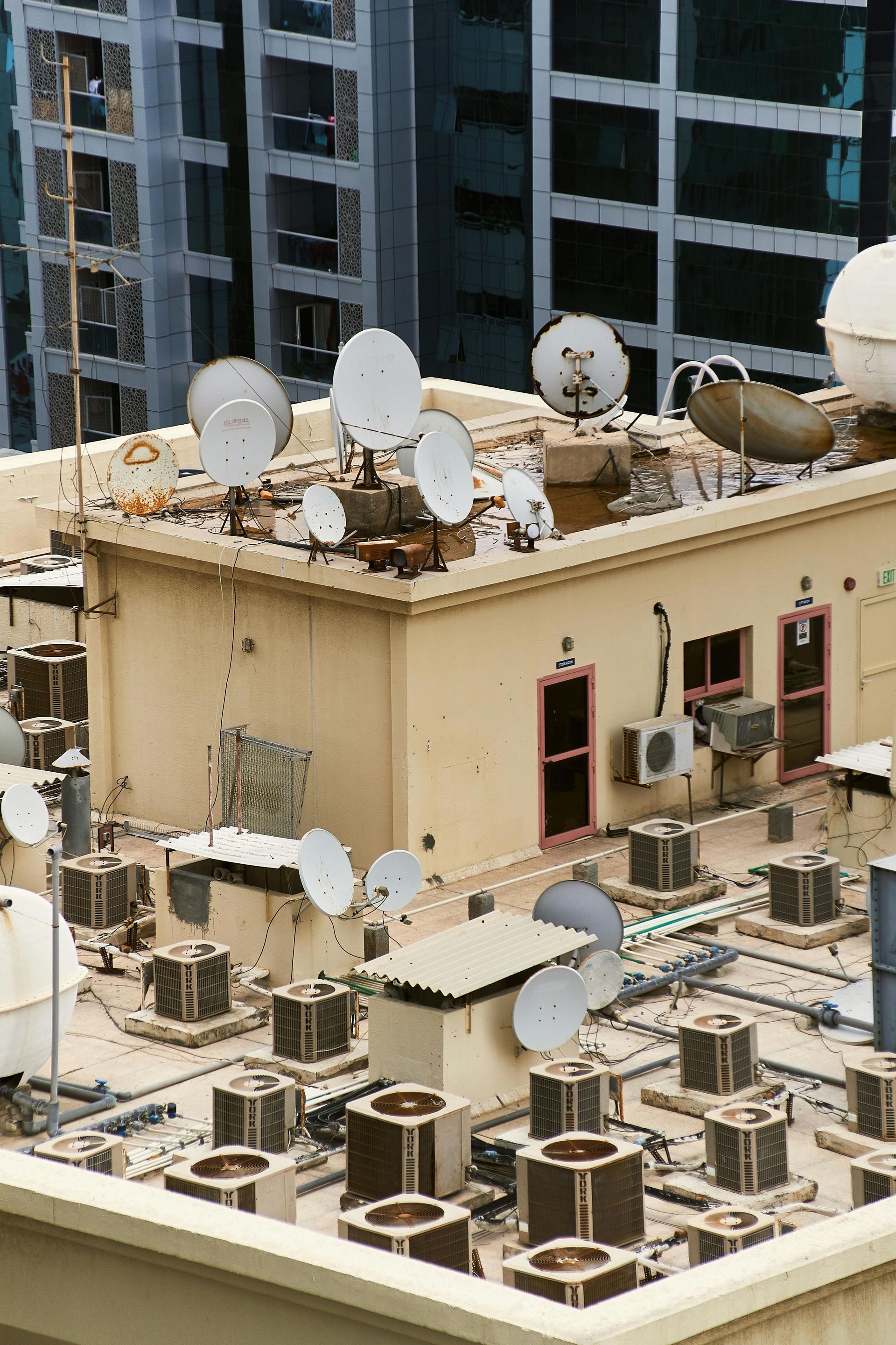 Rooftop with numerous satellite dishes and air conditioning units. Buildings in the background.