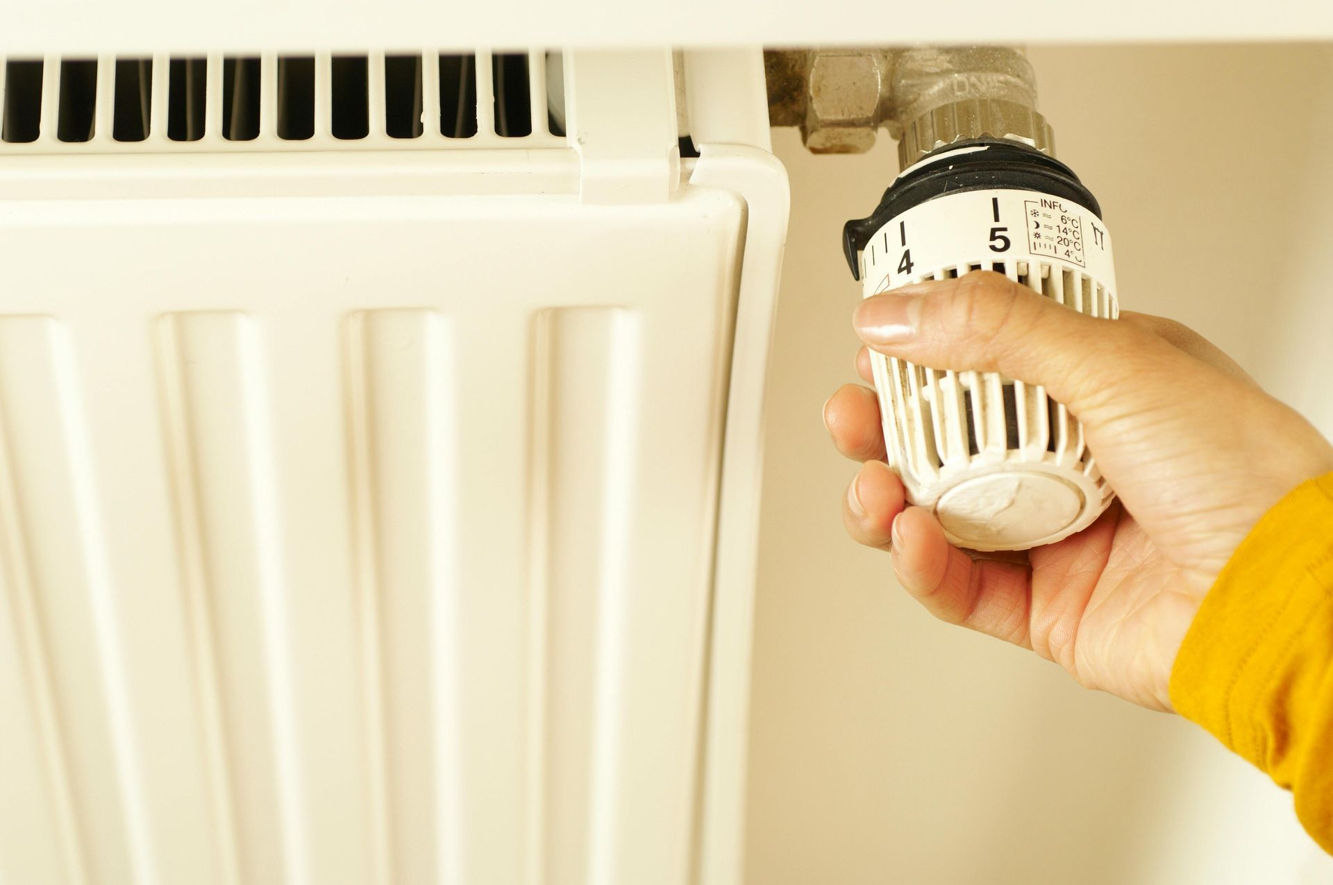 Hand turning a radiator thermostat; white radiator and setting dial.