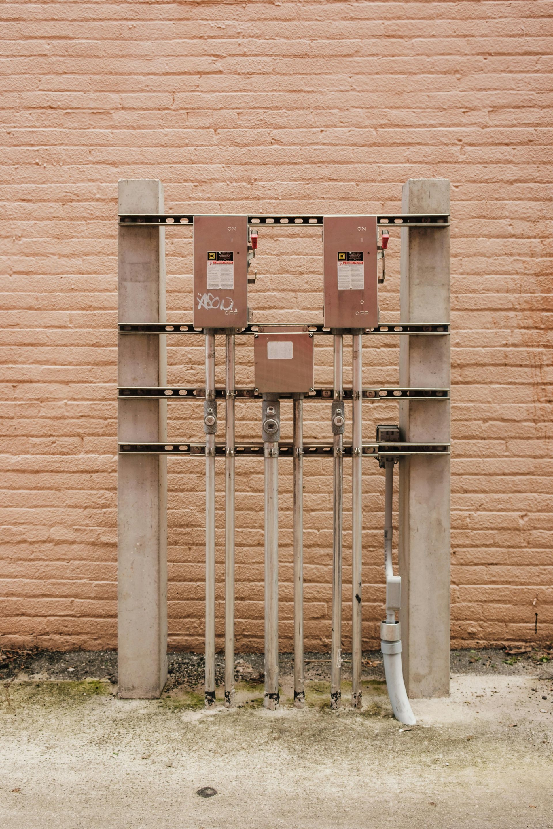 Electrical boxes and conduit mounted on concrete structure against a brick wall.