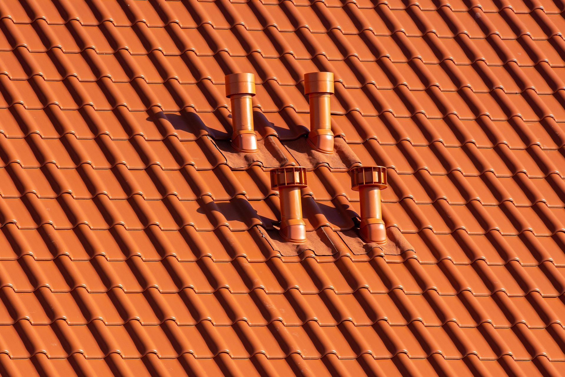Orange tiled roof with four orange vent pipes.