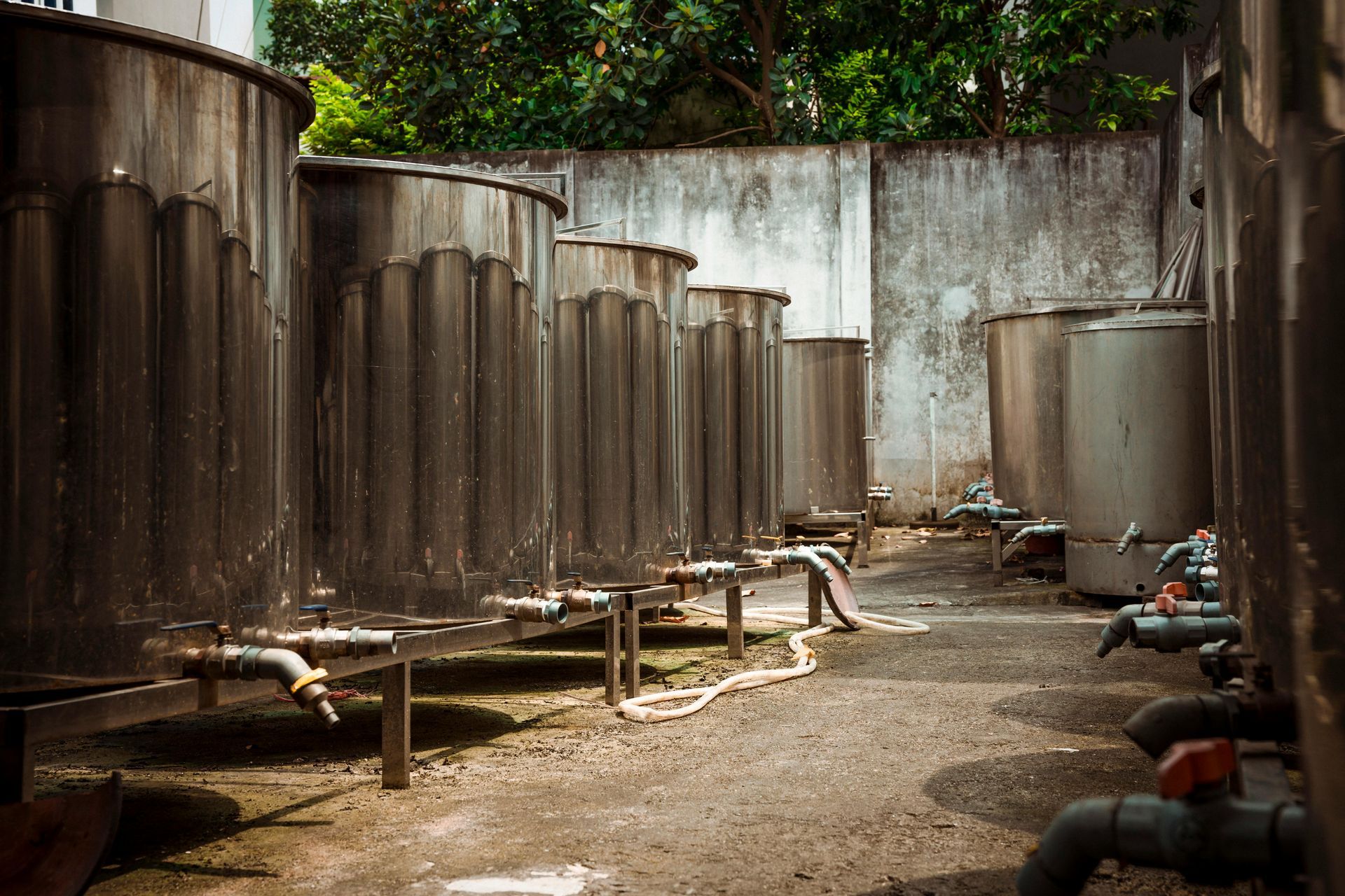 Tanks in an outdoor area. Cylindrical, corrugated metal tanks, pipes, and a concrete wall.